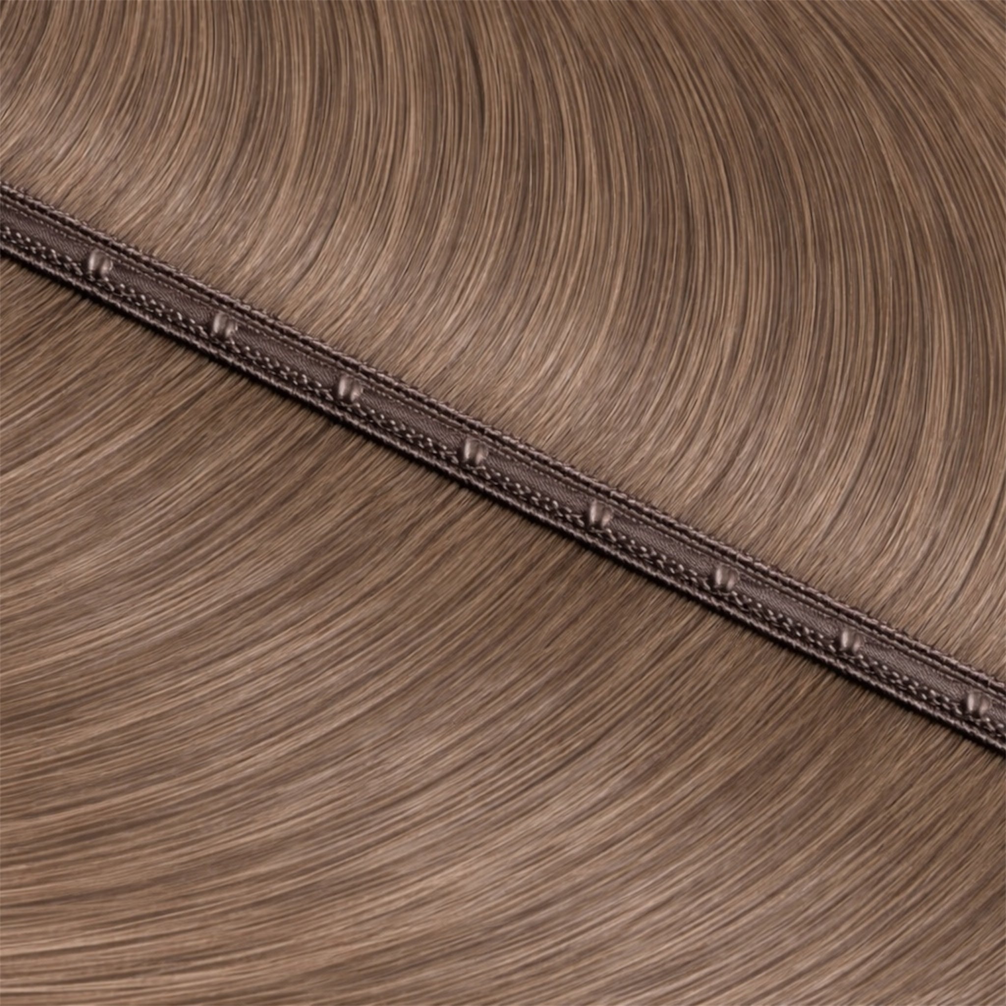 Close-up of  light ashy brown hair extensions with a strip with pu holes in the centre of the base.